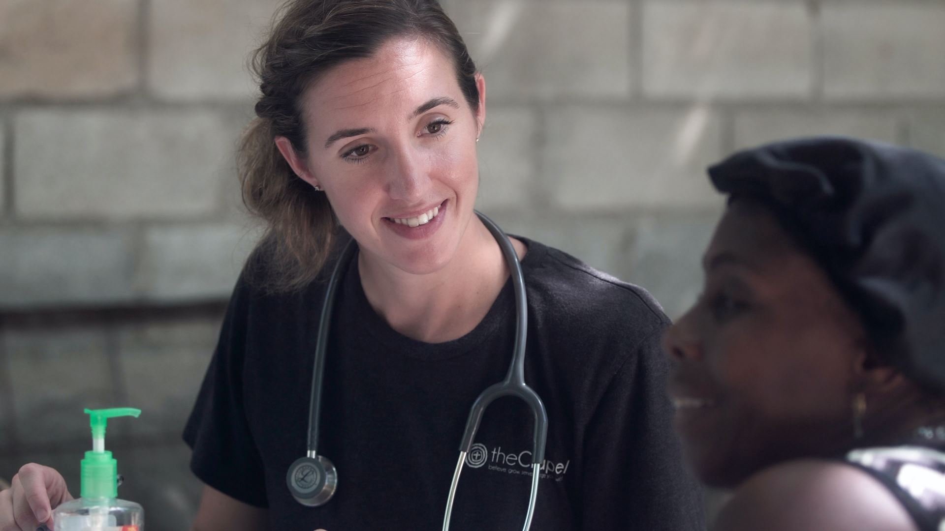 A woman with a stethoscope around her neck smiling at a seated woman