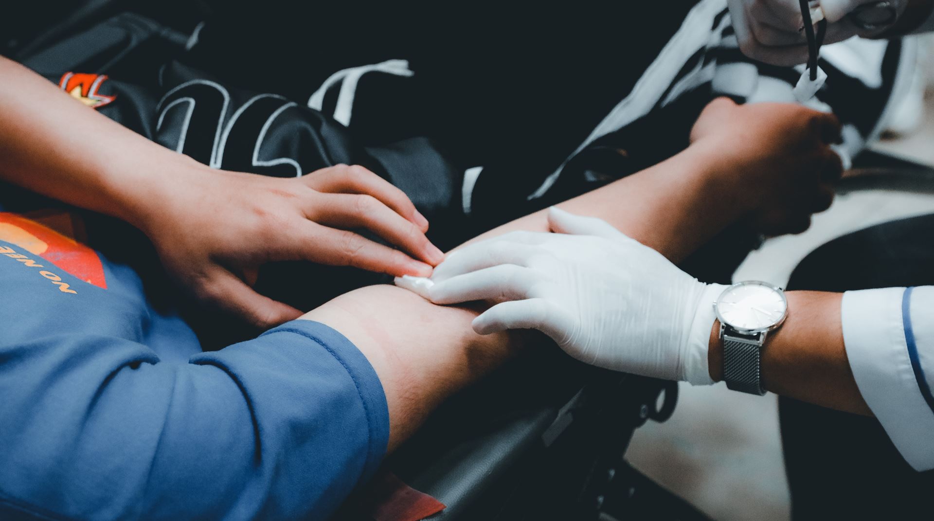 A phlebotomist wearing gloves feels a patient's arm to check for a vein